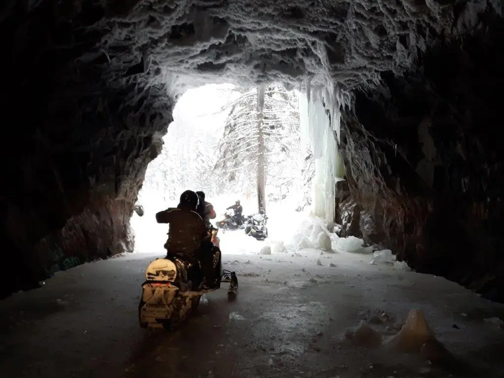 Motoneigistes à l'entrée d'une grotte de glace éclairée par la lumière du jour