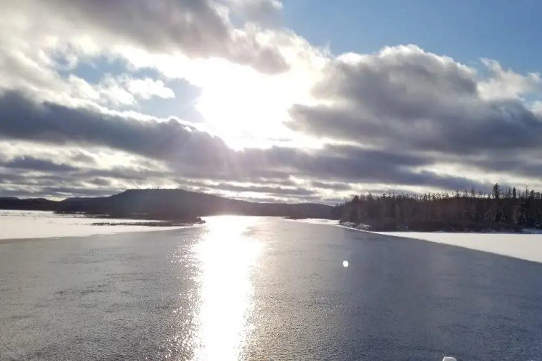 Soleil et nuages sur un lac gelé bordé de forêt