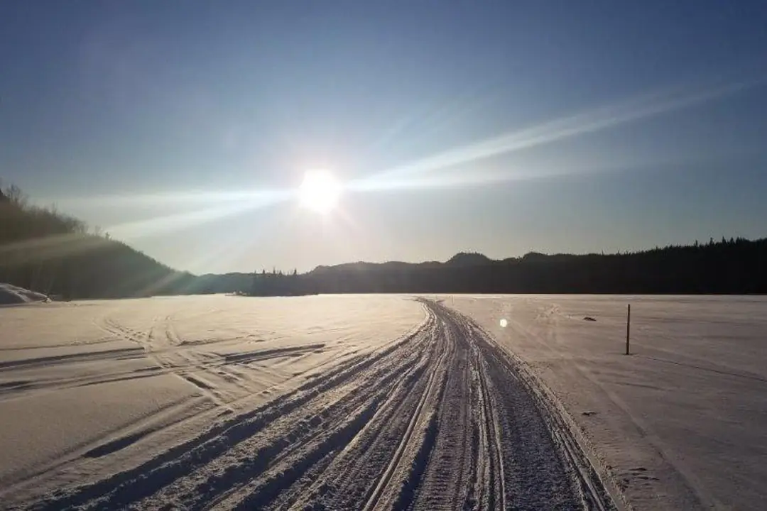Trace de motoneige sur un lac gelé, soleil bas à l'horizon